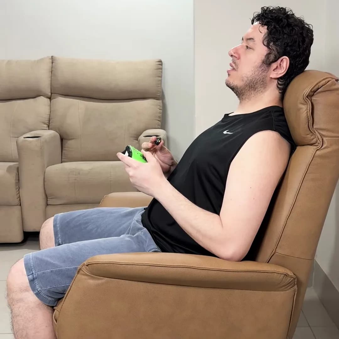 Bruno jogando videogame com o controle na mão, sentado na Poltrona Levita Damie em couro caramelo